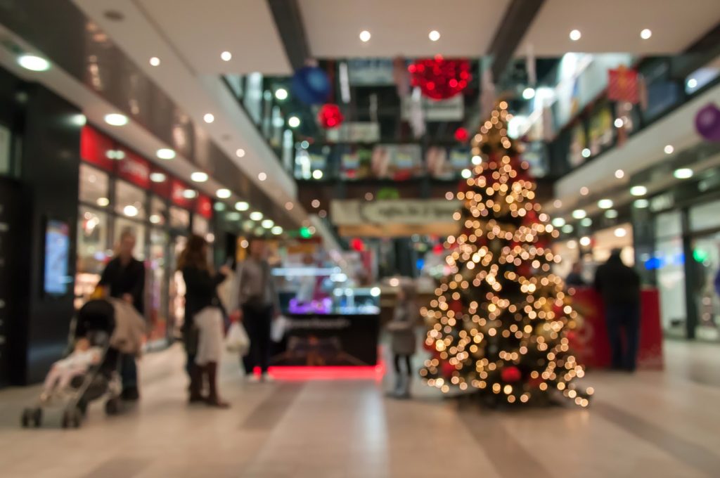 Inside large indoor retail mall with cell phone store blurred in the background a lit Christmas tree on display